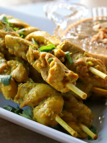 Keto chicken satay on skewers on a white serving dish with peanut sauce