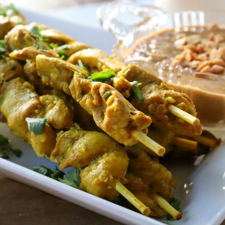 Keto chicken satay on skewers on a white serving dish with peanut sauce