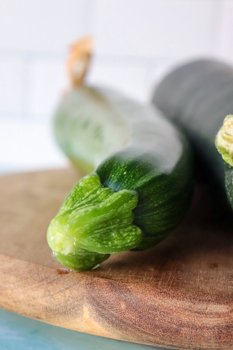 Front view of a zucchini on a wooden block next to a darker green zucchini
