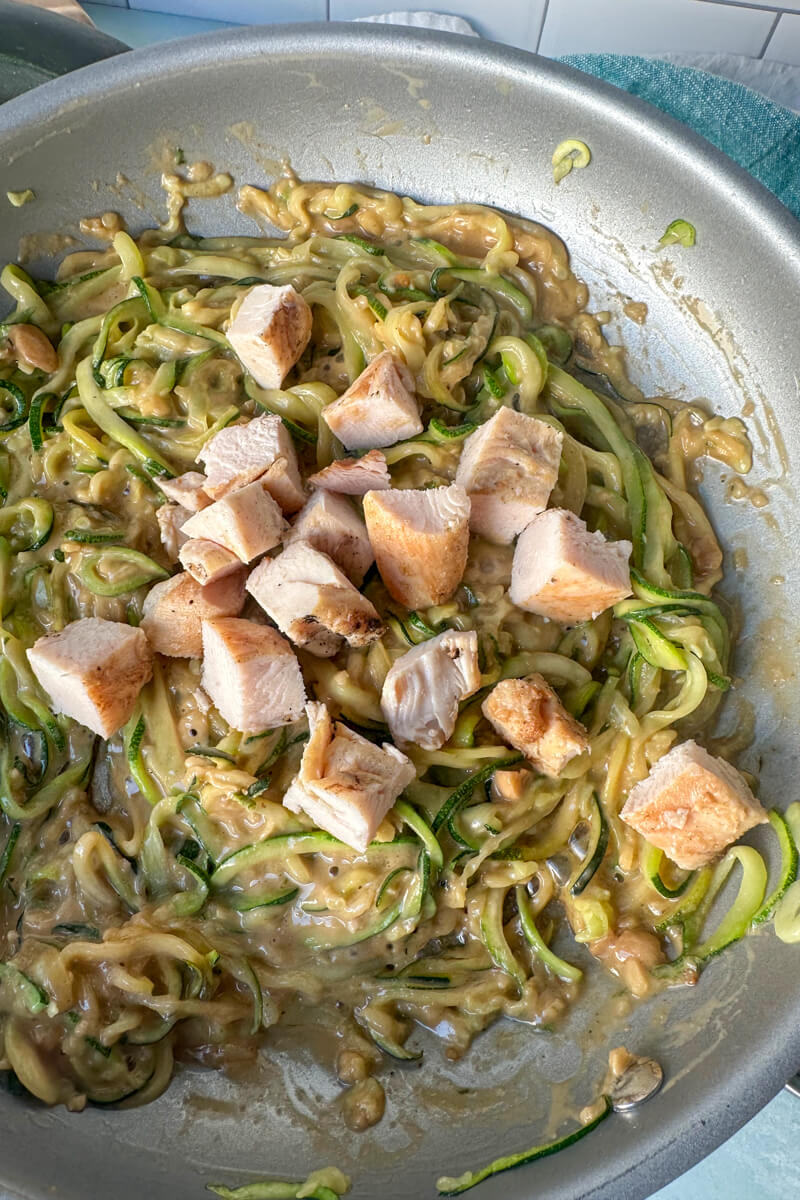 Overhead view of a metal skillet cooking zoodles with Thai peanut sauce and chicken