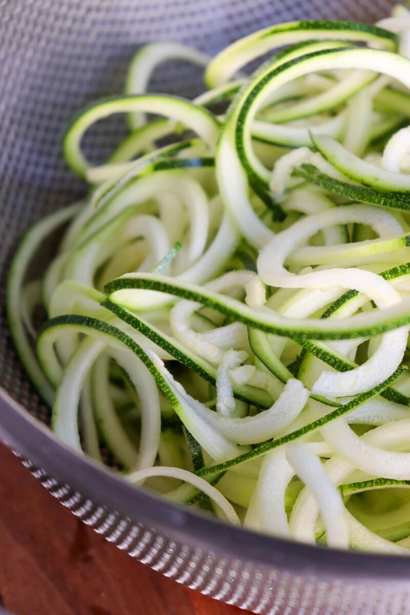 Close up view of a metal colander with spiralized zucchini noodles