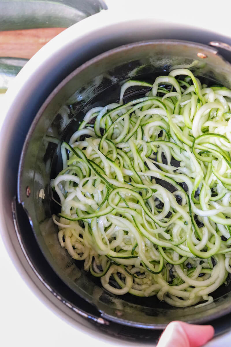Overhead view of a metal air fryer with spiralized zucchini noodles