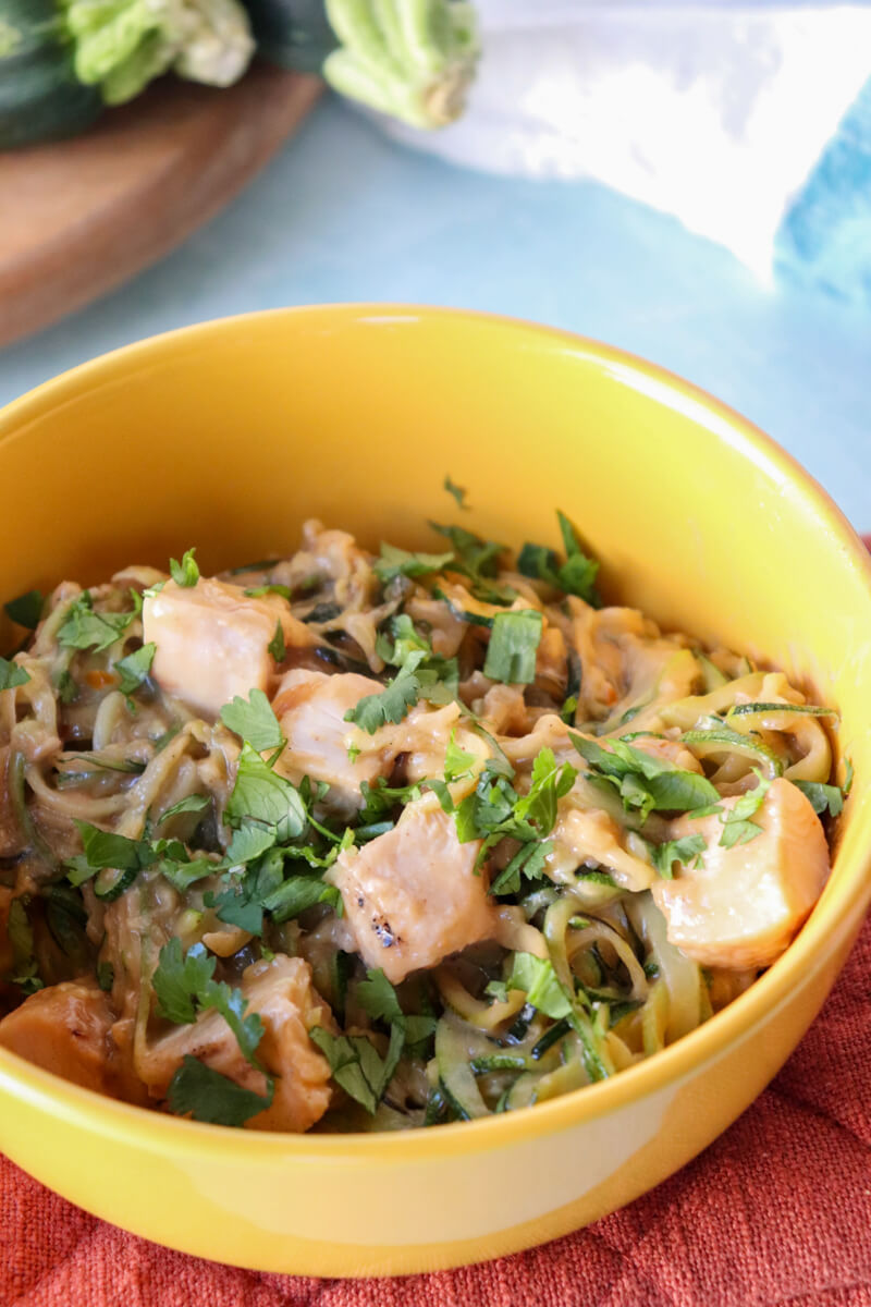 A yellow bowl of Thai peanut and chicken zoodles with cilantro