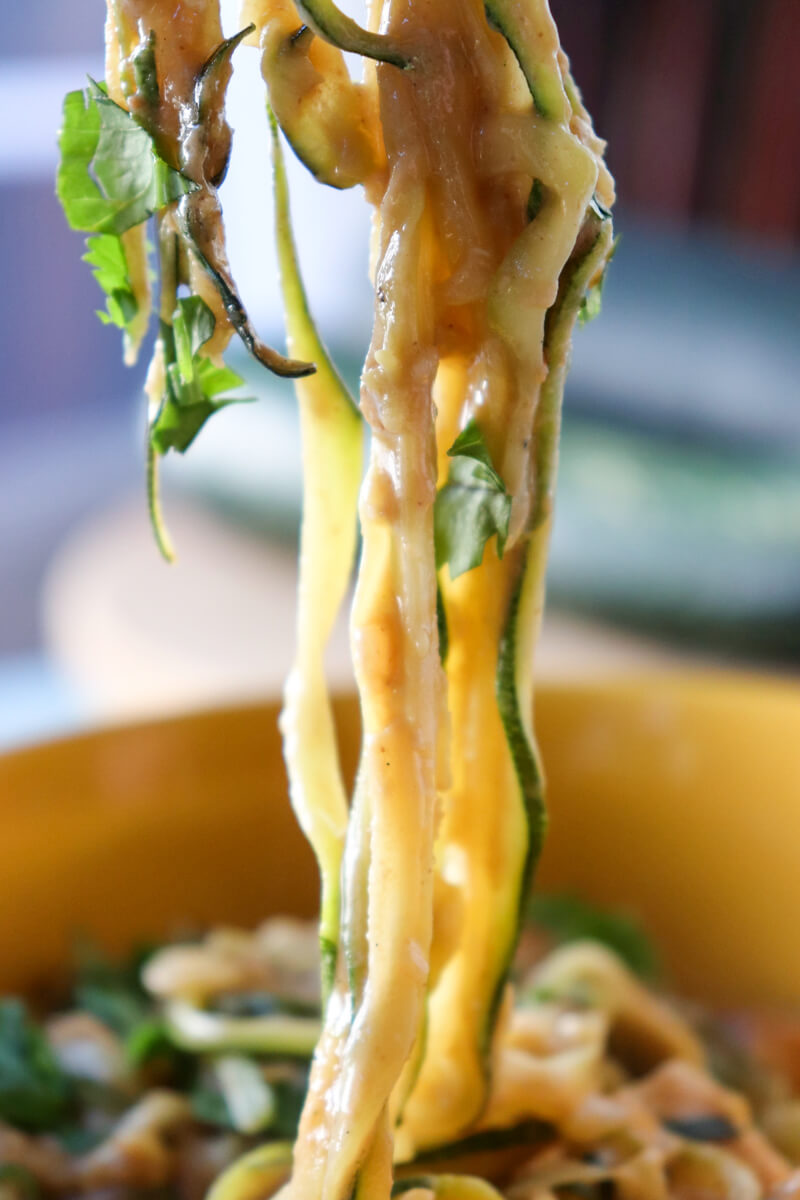 Zoodles, or zucchini noodles with Thai peanut sauce and cilantro, being lifted out of a bowl