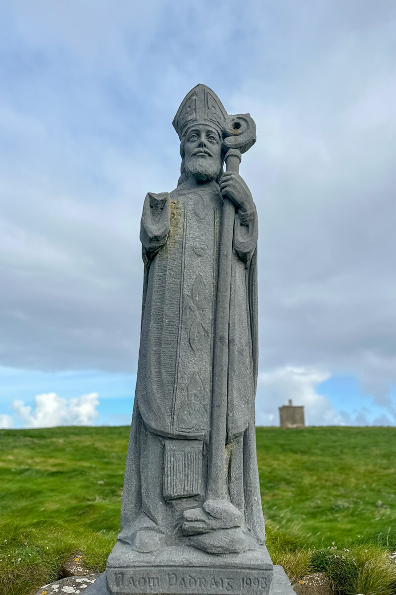 Stone statue of St. Patrick at Downpatrick Head in front of a field of grass