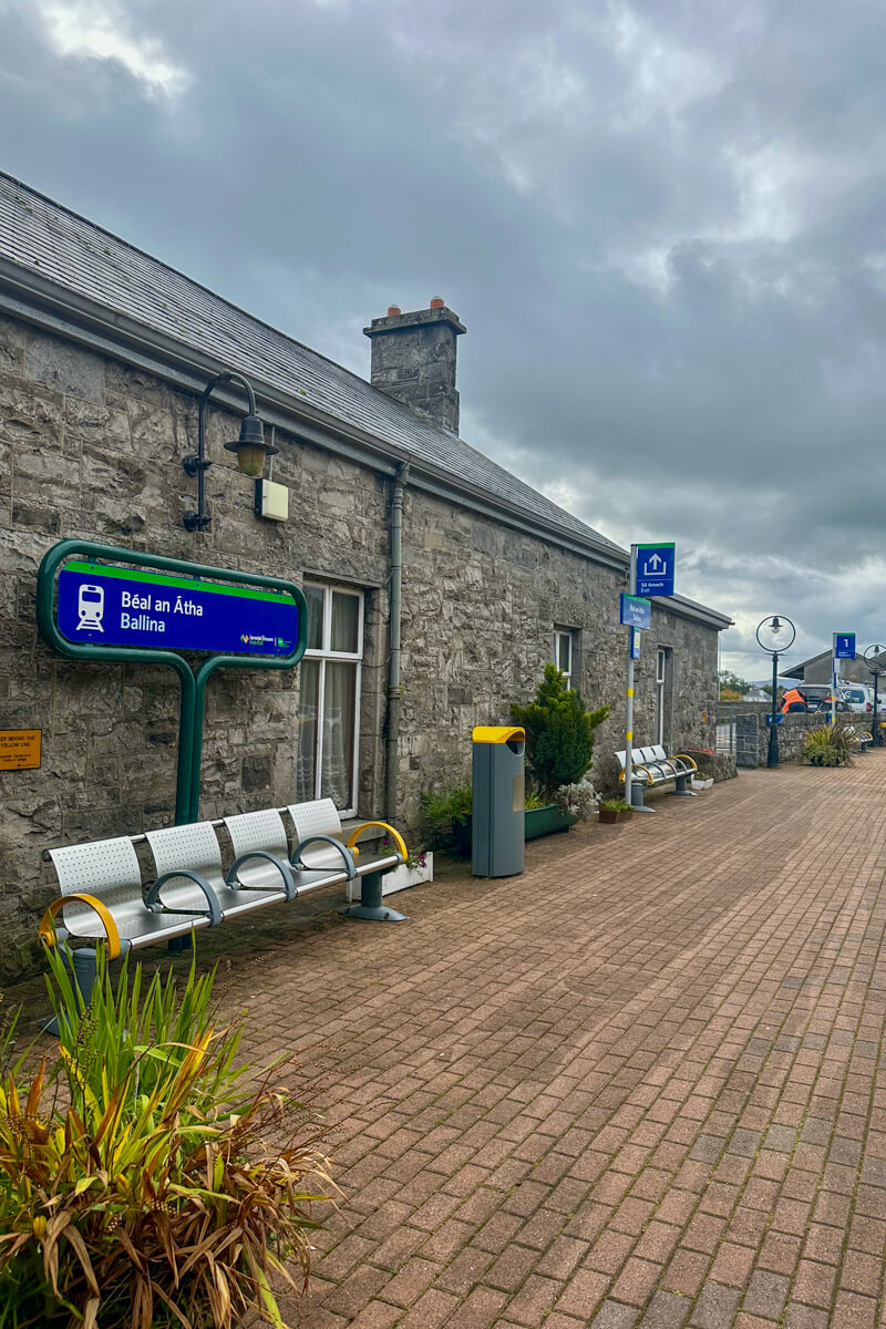 View of the stone building and chairs with a blue sign at the Ballina Train Station in Ireland