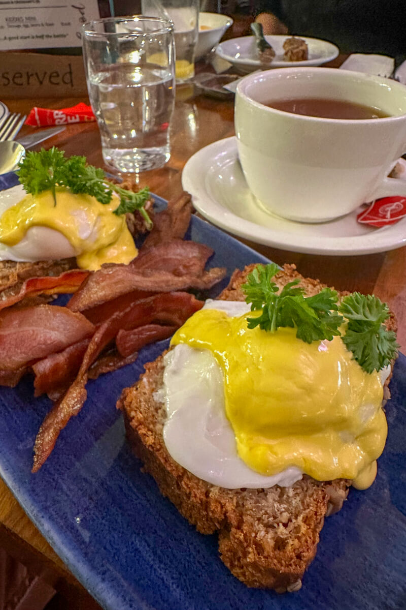 Front view of an eggs Benedict on Irish brown bread with bacon and a cup of tea.
