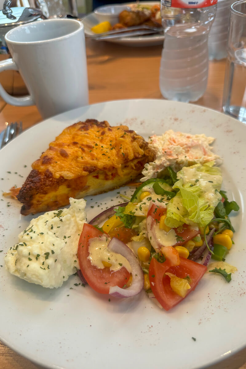 A plate of food with quiche covered with cheddar cheese and salads next to it.
