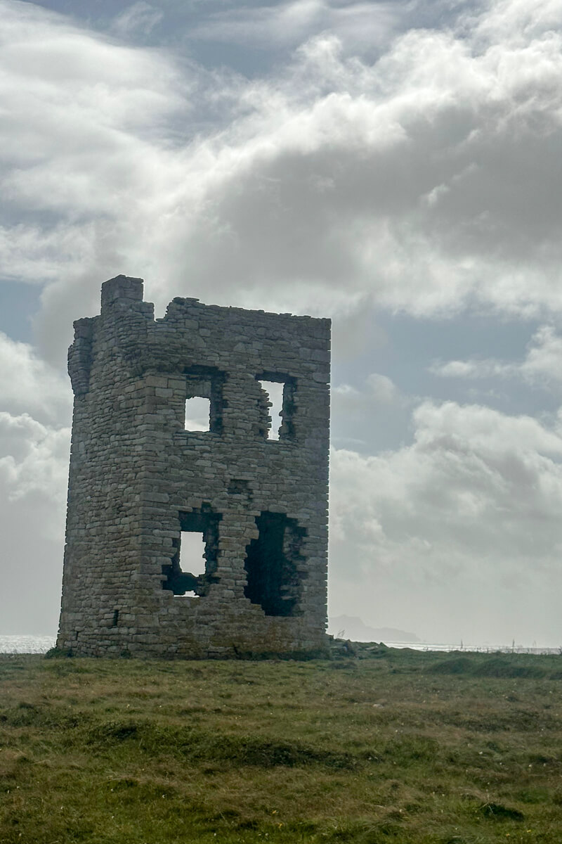 A view of Glosh Tower in Letterbeg, Ireland on a hill with clouds in the background.