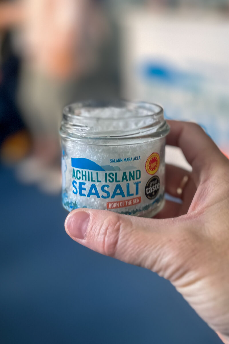 A hand holding up a small glass jar of Achill Island Sea Salt
