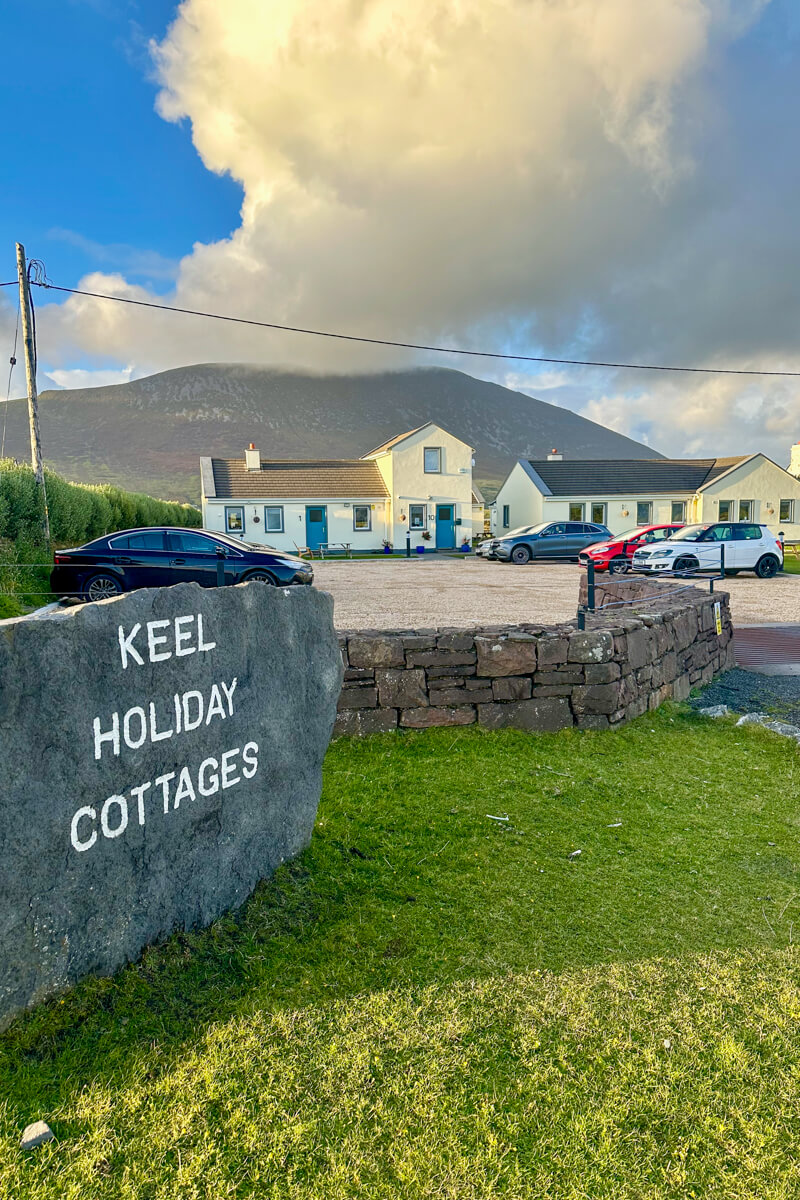 A sunny late afternoon view of Keel Holiday Cottages, a stone sign and the cottages in the background