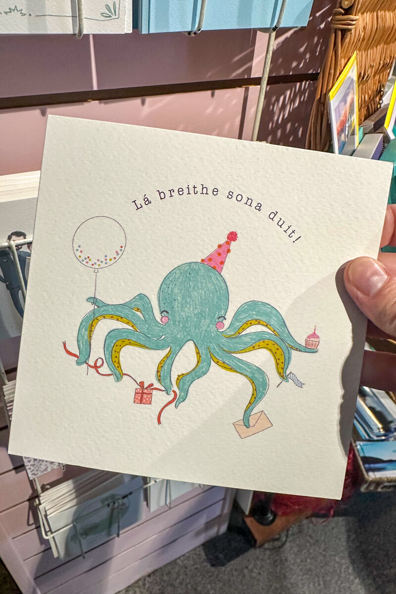 A birthday card in Irish language with an octopus wearing a hat.