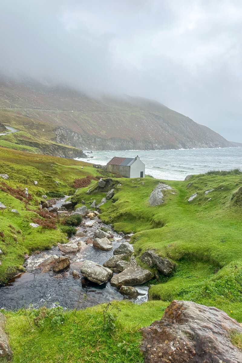 A view of a small rocky stream leading down to a white cottage on Keem Beach