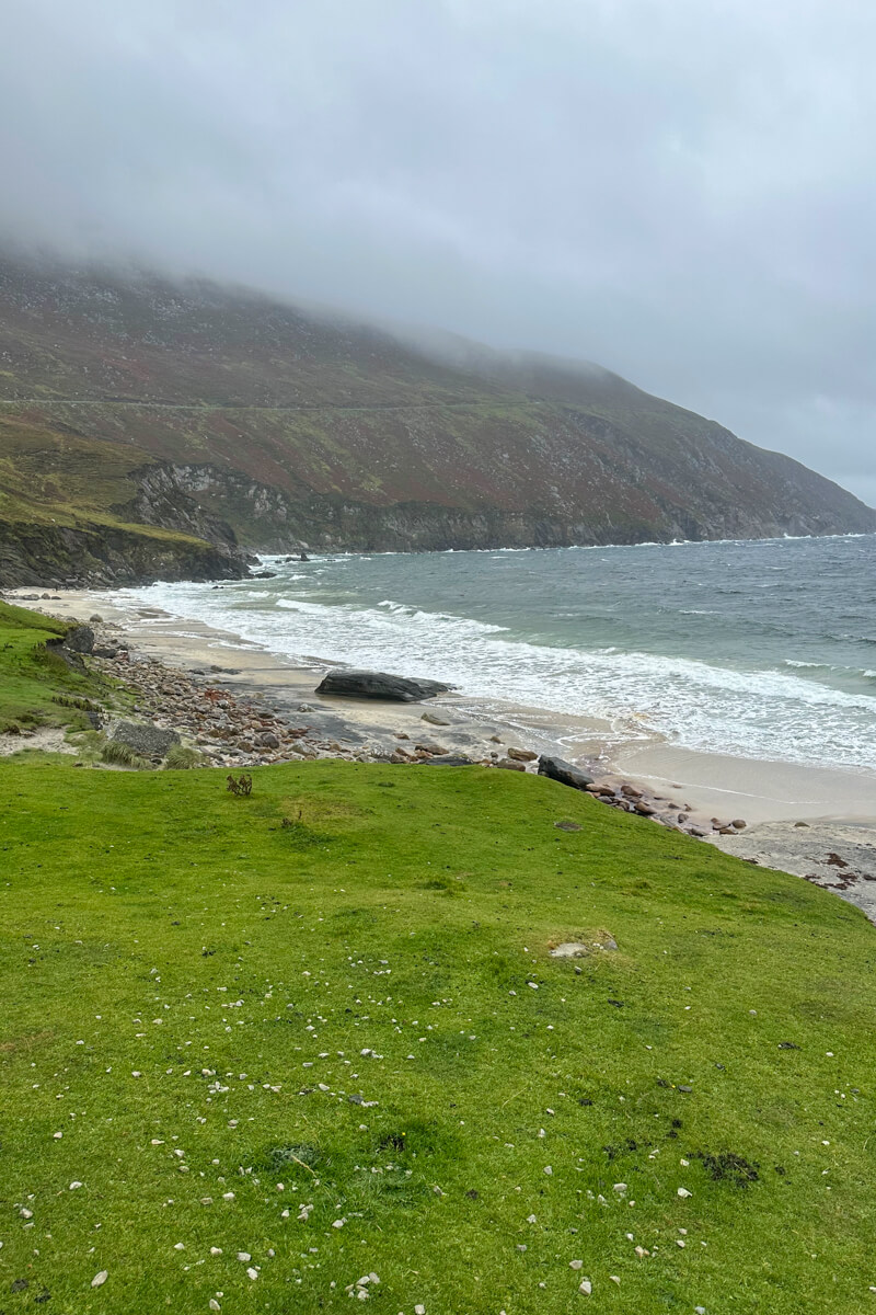 Grassy area in front of Keem Beach with dark hills in the distance and the clouds and mist coming down