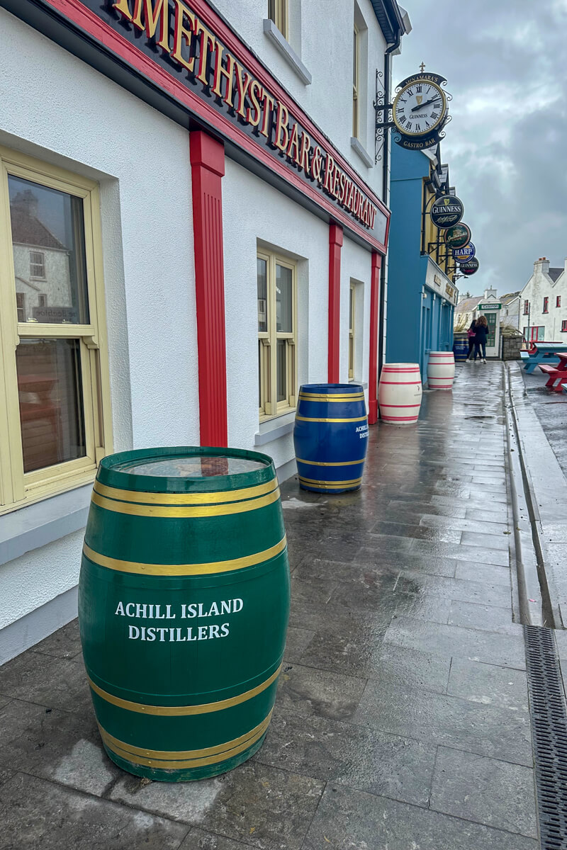 A view of the stree with white and red painted buildings and green barrels lined up along it.