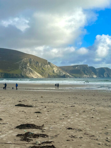 Keel Beach, Mayo Ireland with sand, reddish seaweed, water in the distance and hills beyond the water.