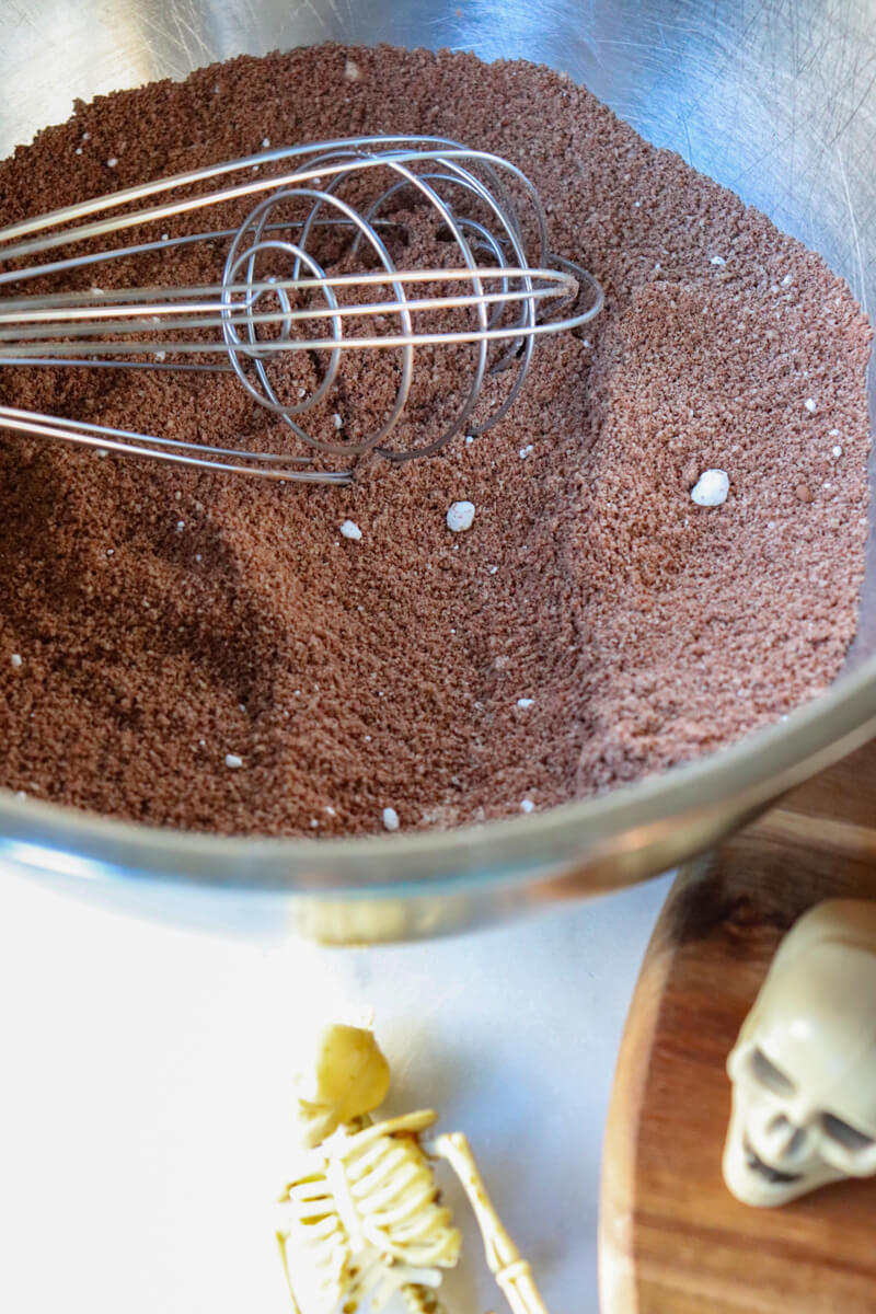 A metal bowl with a whisk mixing the dry ingredients for the keto chocolate crust.