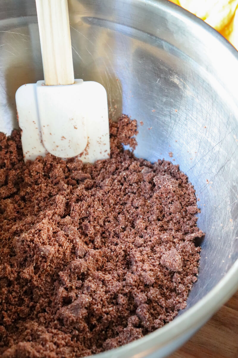 Closeup view of the crumbly sugar free chocolate crust mixture with a white spatula in it.