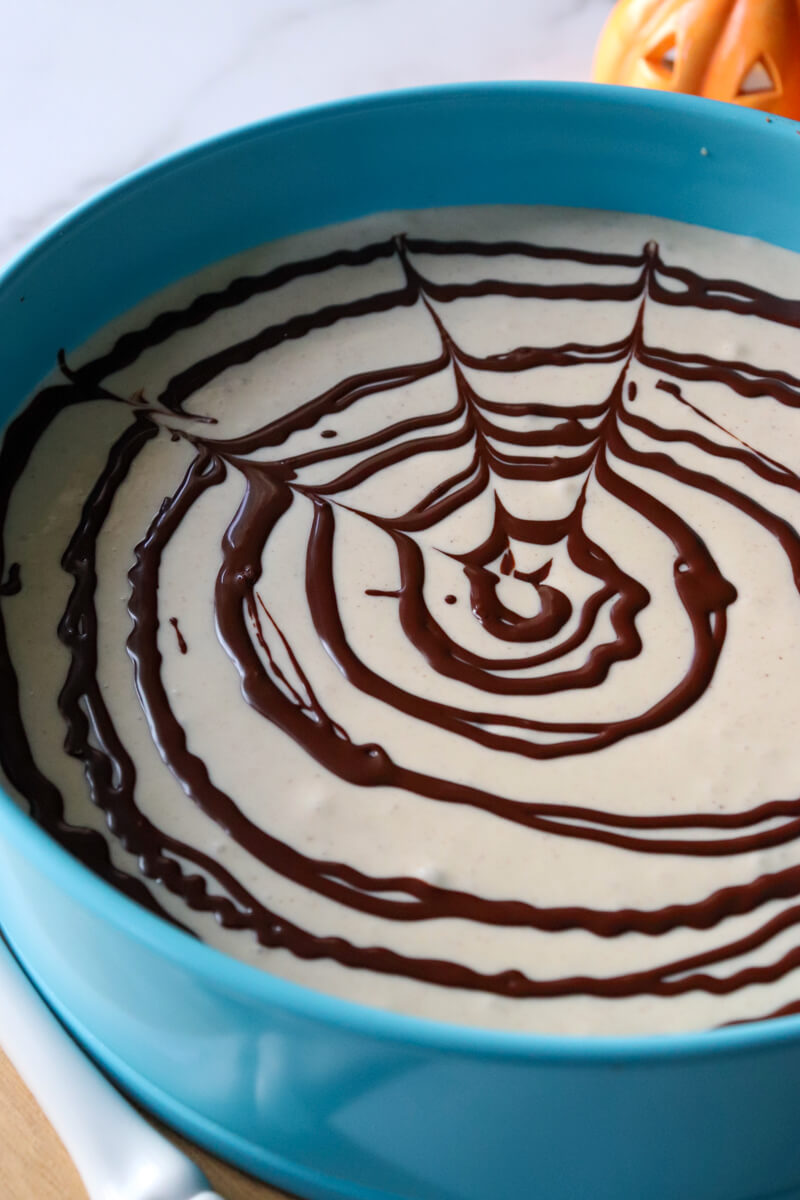 Cheesecake with spider web pattern being put on top with chocolate.