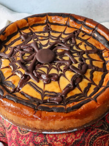 Front overhead view of a low carb eggnog cheesecake on a pedestal with a chocolate spider web perfect for Halloween