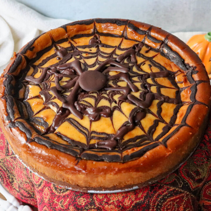 Front overhead view of a low carb eggnog cheesecake on a pedestal with a chocolate spider web perfect for Halloween