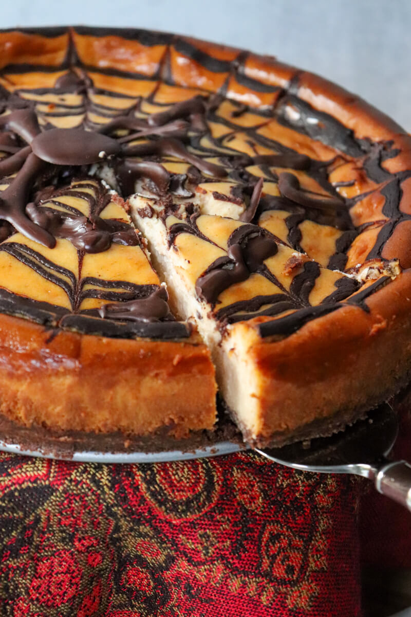 Closeup of a Keto eggnog cheesecake with a chocolate spider and web with a piece being taken out.