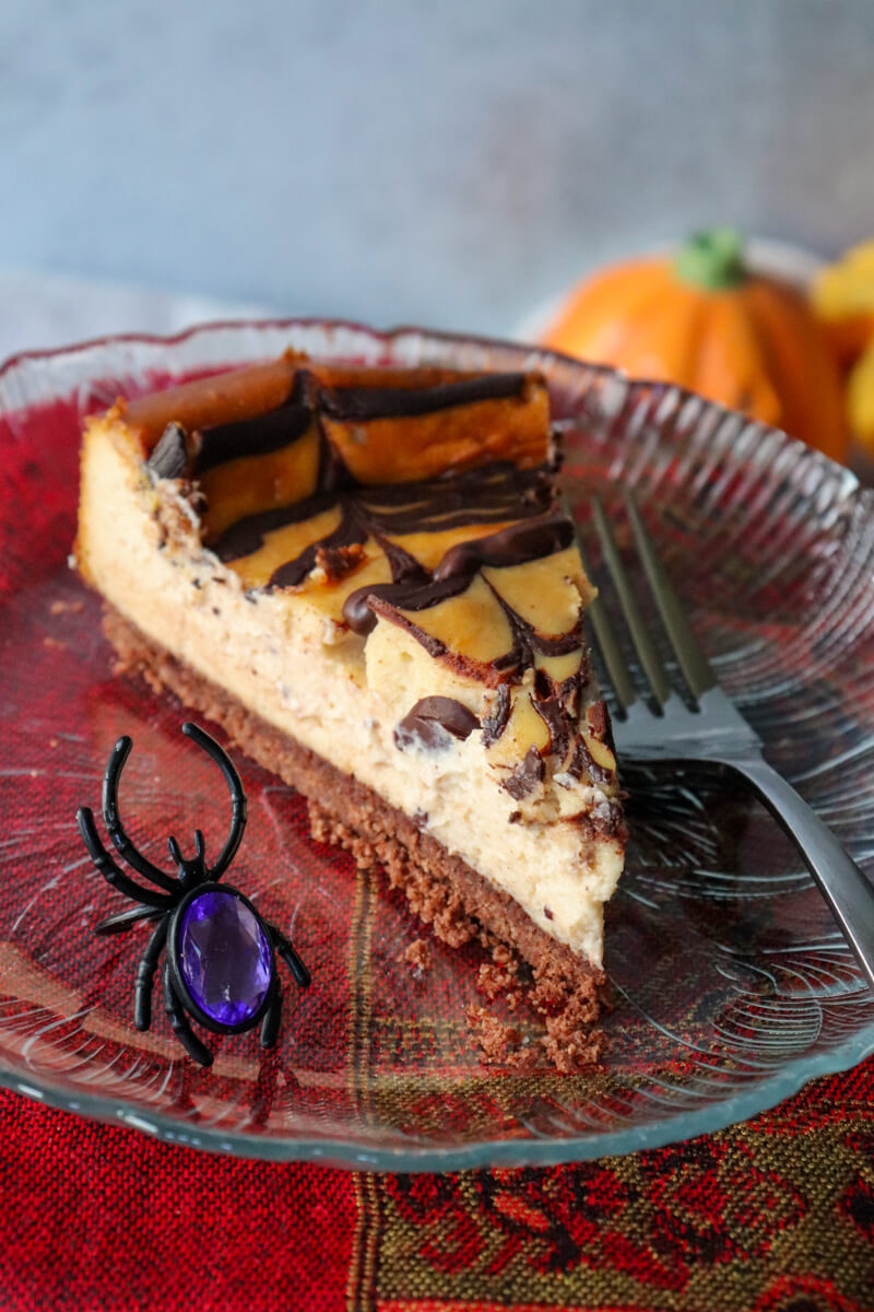 A piece of keto eggnog cheesecake on a glass plate with a fork and plastic spider next to it.