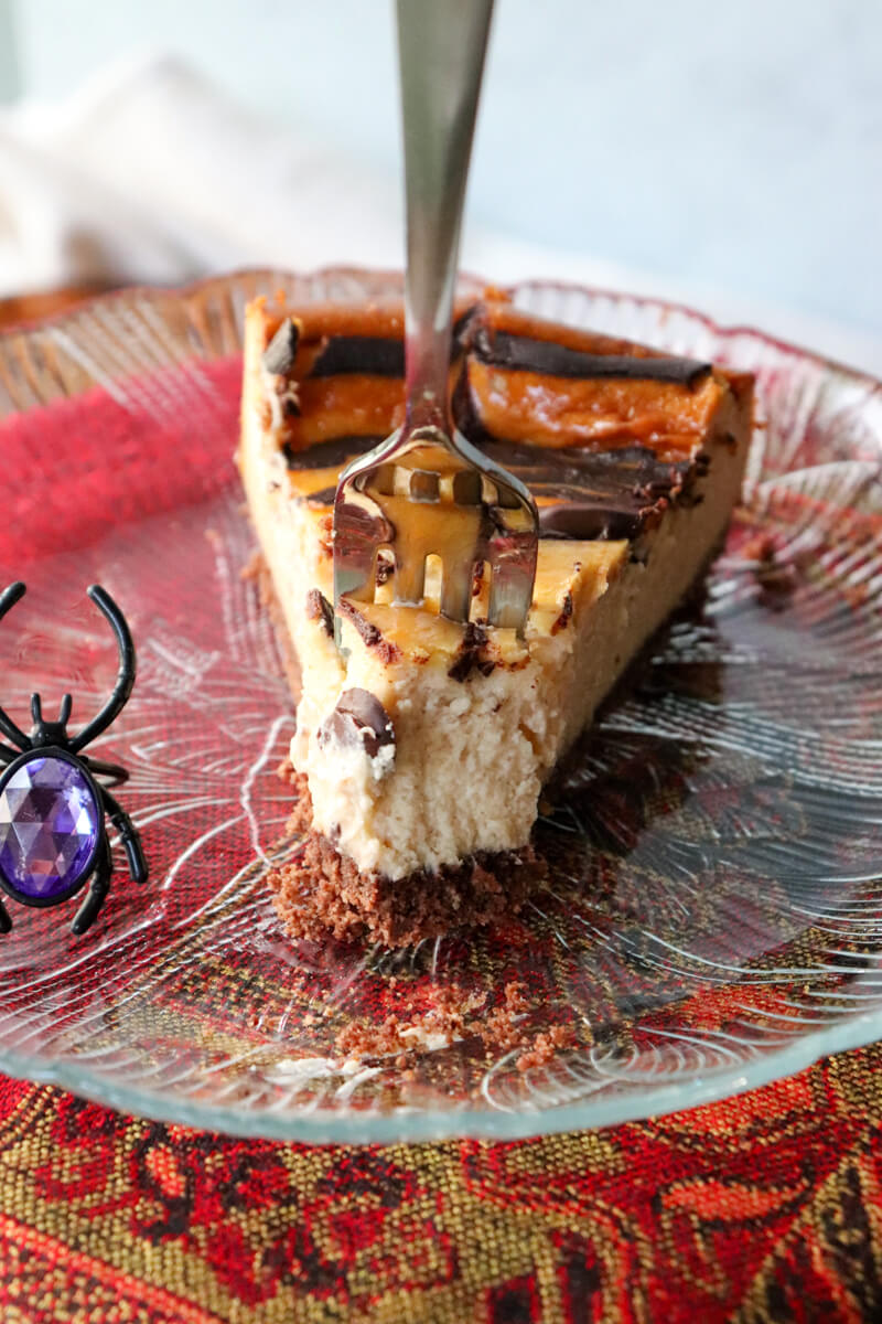 A piece of low carb Halloween dessert, eggnog cheesecake, with a fork in it on a glass plate ready to take out a bite.