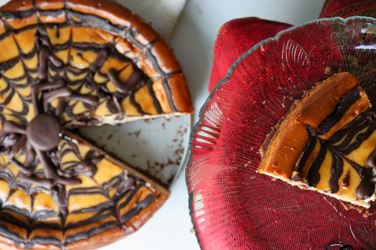 Overhead view of a Keto eggnog cheesecake with a chocolate spider and web and a piece taken out.