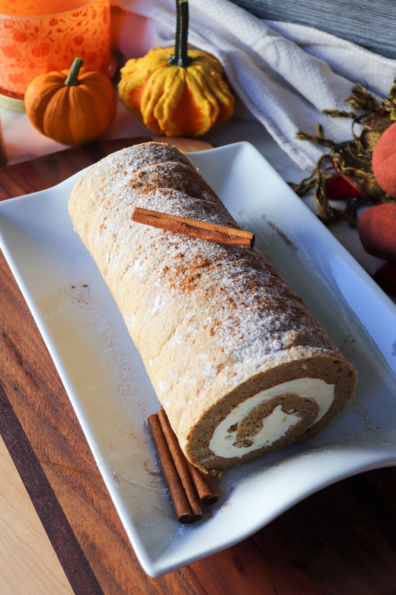 Front view of the keto pumpkin roll on a rectangular white plate with a cinnamon stick on top