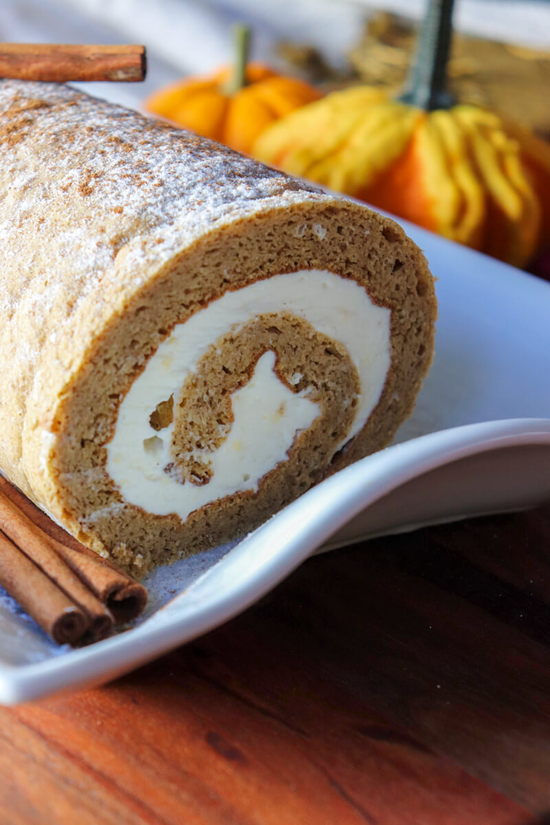 Front view of the keto pumpkin roll on a rectangular white plate with a cinnamon stick on top