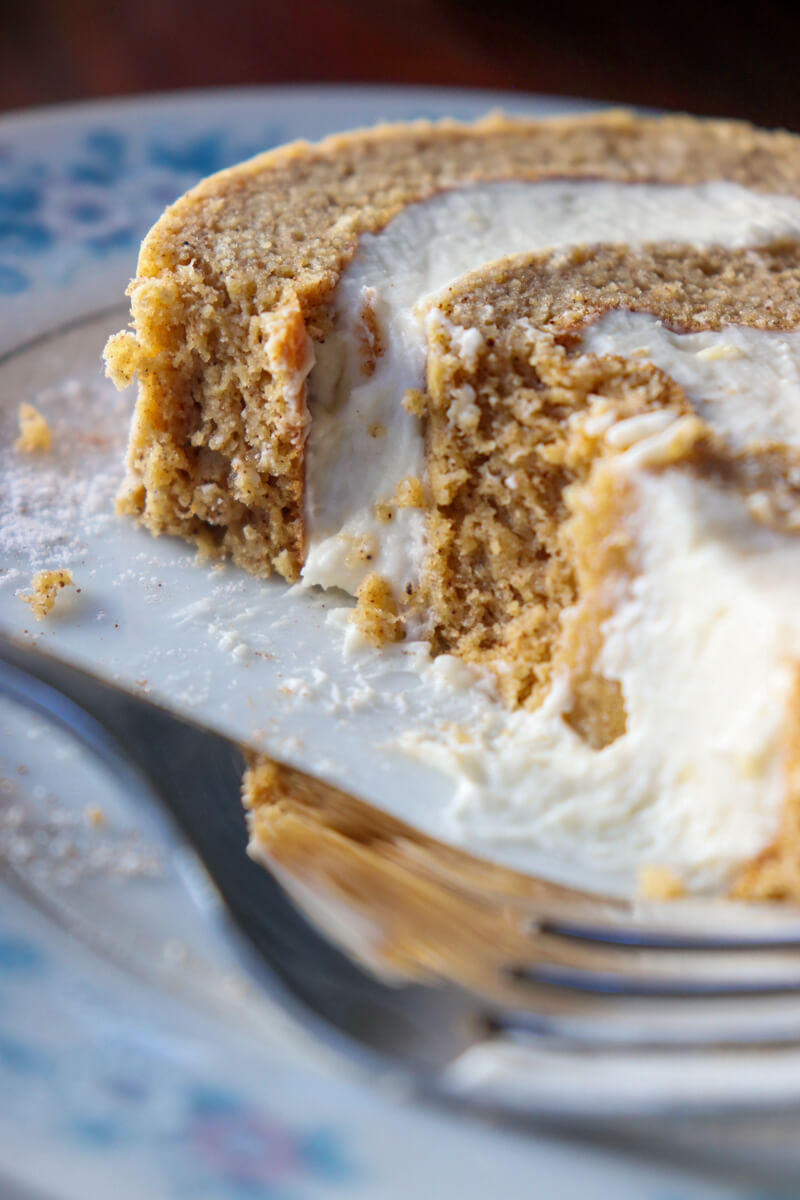A closeup of a piece of low carb pumpkin roll on a vintage china plate with blue flowers, partially eaten, with a fork on the plate