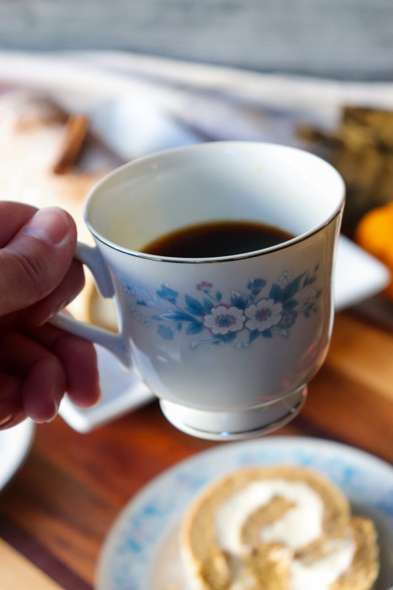 A hand holding up a vintage teacup with blue flowers holding coffee