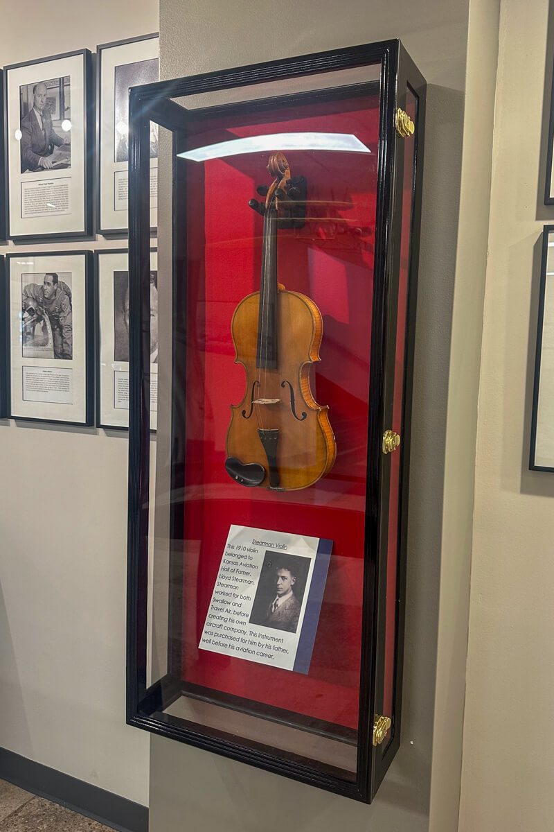 A violin in a glass display on a white background in the Kansas Aviation Museum