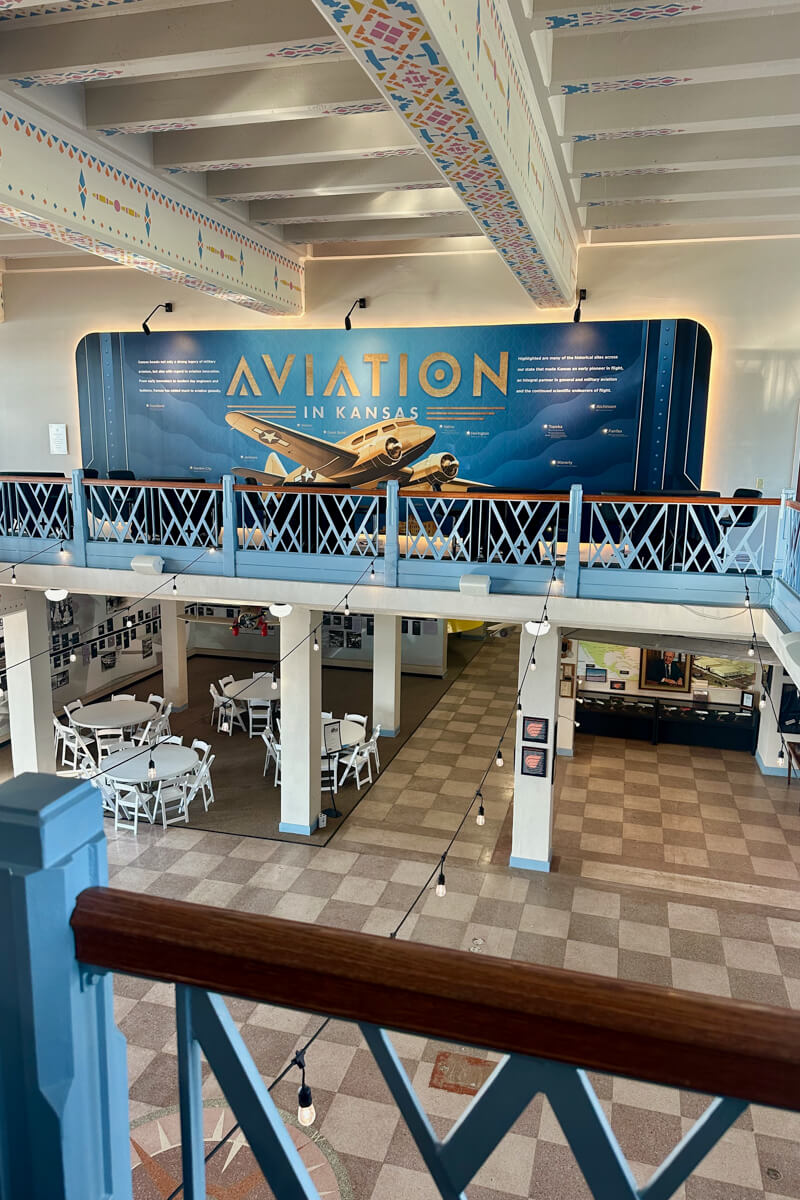 A view looking out over the balcony inside the museum over looking the checked art deco floor looking across at a blue aviation poster with a large airplane