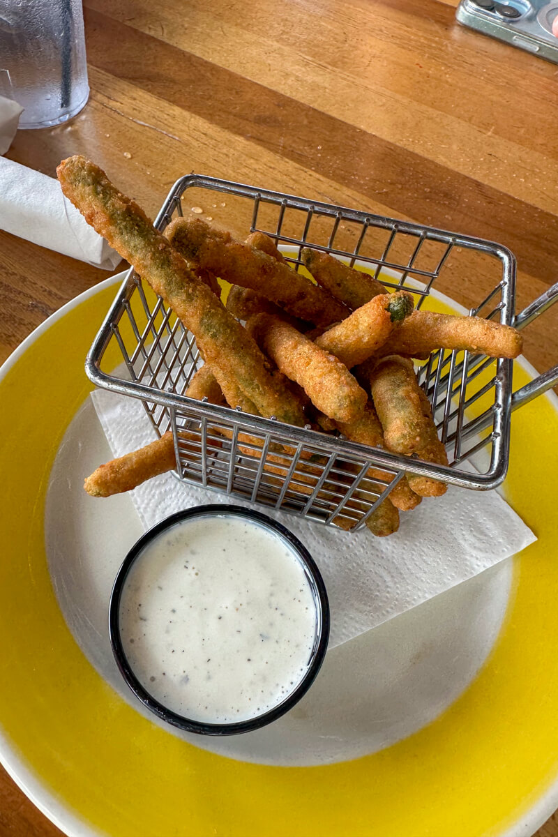 Overhead view of a metal basket fried green beans and a small container of ranch dressing