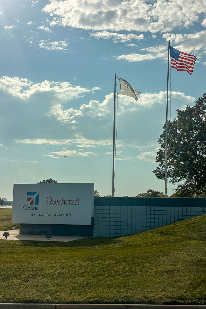 A US flag and another white flag flying over a Beechcraft, Textron sign