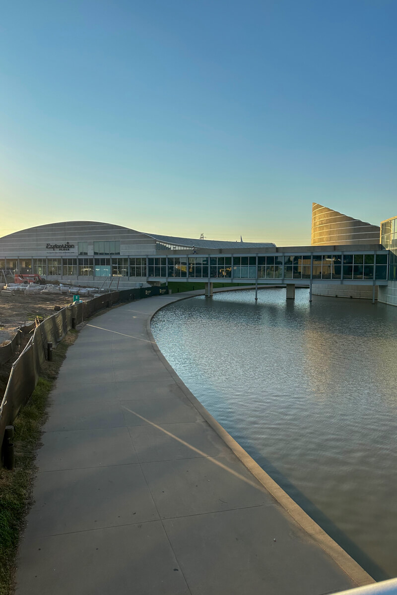 A walkway along the water leading to the Exploration Place building lined with windows