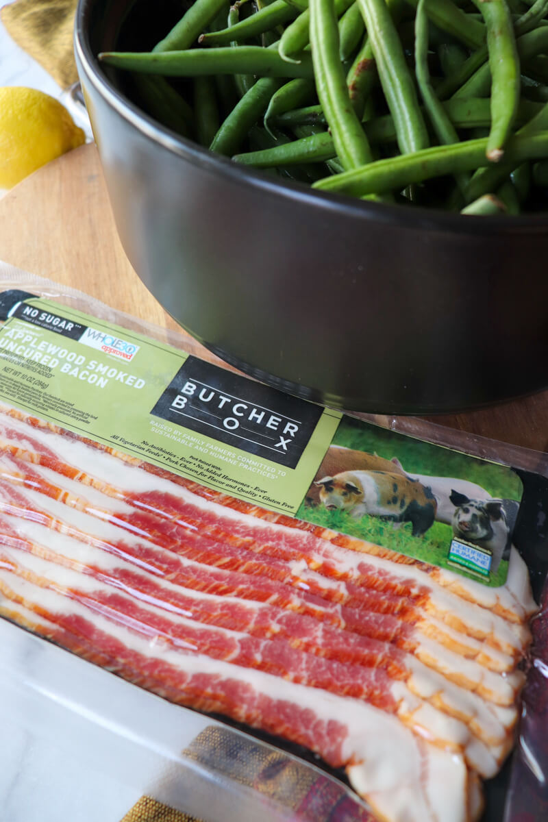 Black pan of raw green beans with a package of ButcherBox bacon