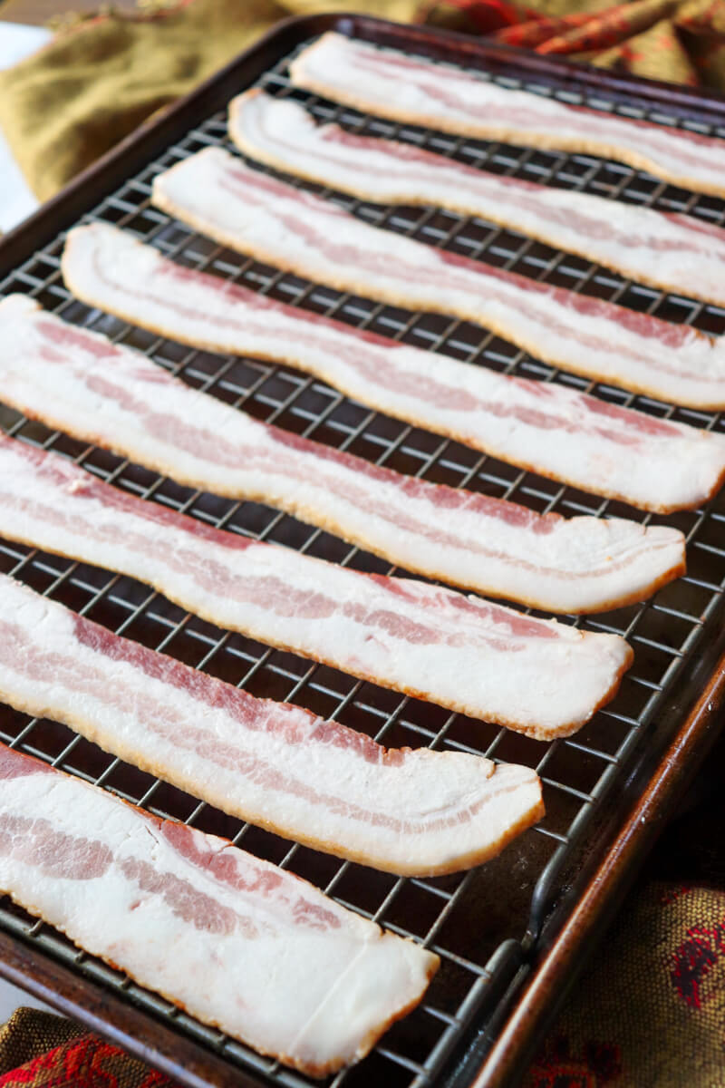 Front view lined up uncooked bacon on a baking pan with grill
