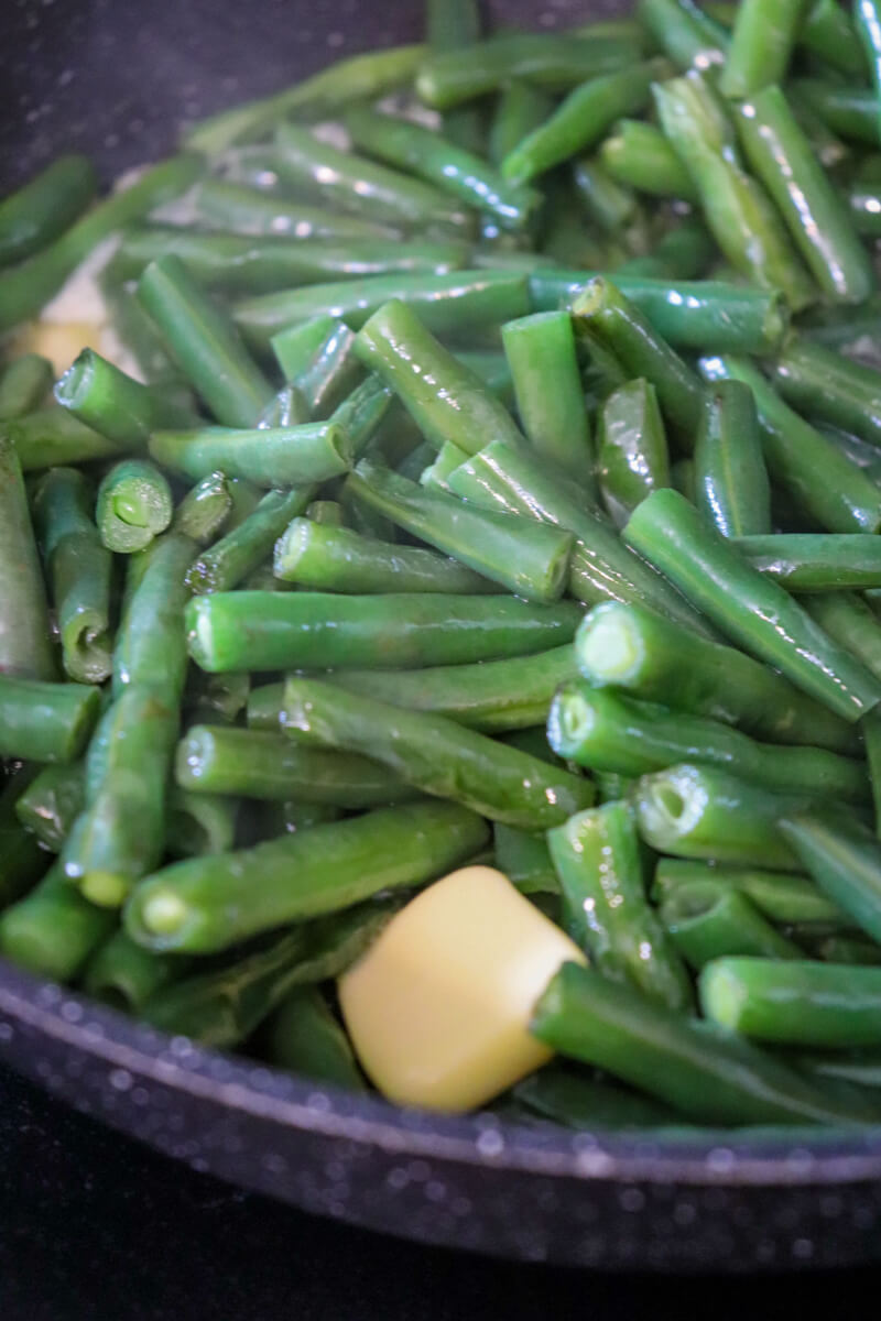 Close up of a black skillet with green beans and butter