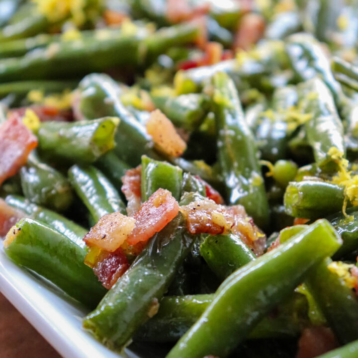 Close up view of green beans with bacon on a white serving dish with lemon zest