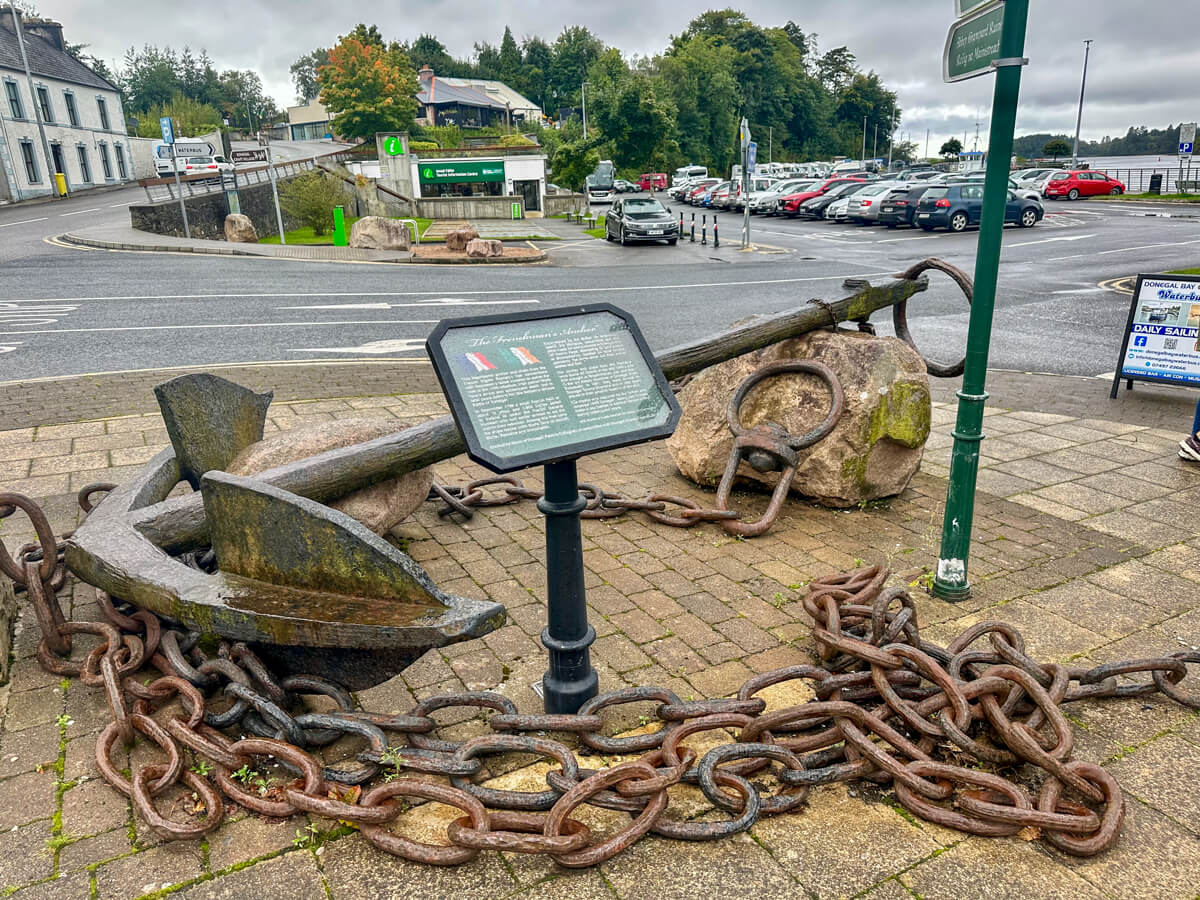 A giant chain and anchor on a cobblestone walkway with a green information sign