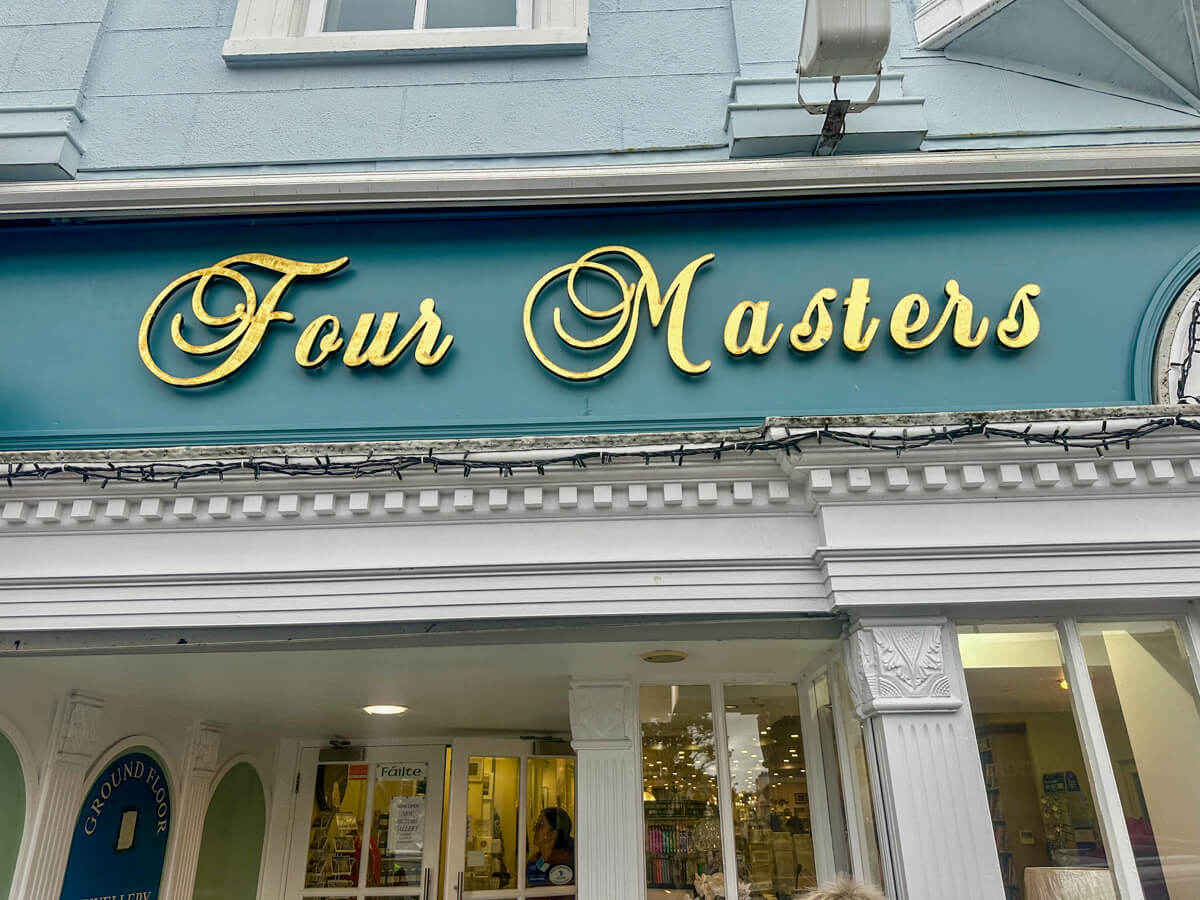 A green storefront sign in gold cursive that says Four Masters