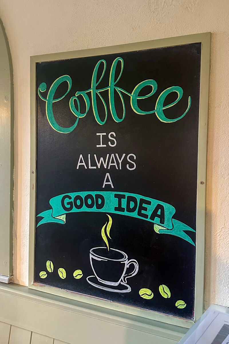 A black background sign written in teal and white that says "Coffee is always a good idea" with a picture of a coffee cup