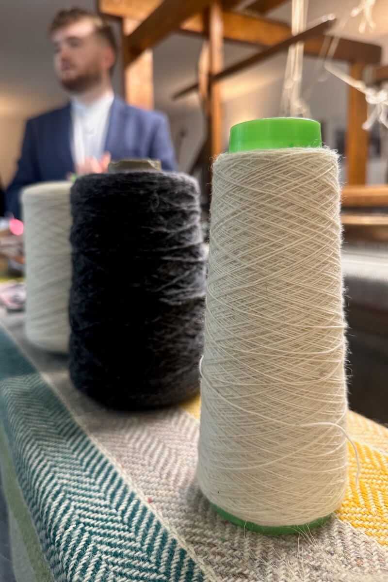 Spun wool skeins sitting in front of the wool loom and a man in a blue tweed coat in the background