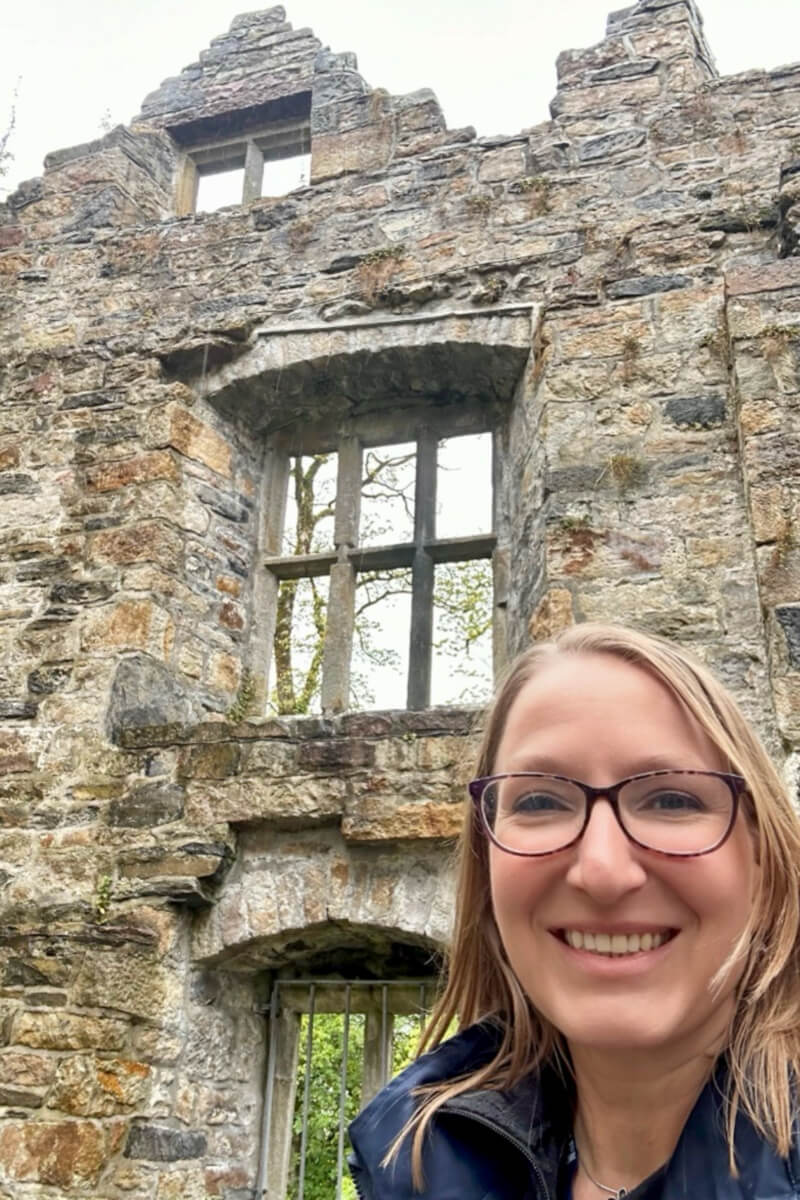 A blond woman wearing glasses in front of the Donegal Castle stone wall and window overhead