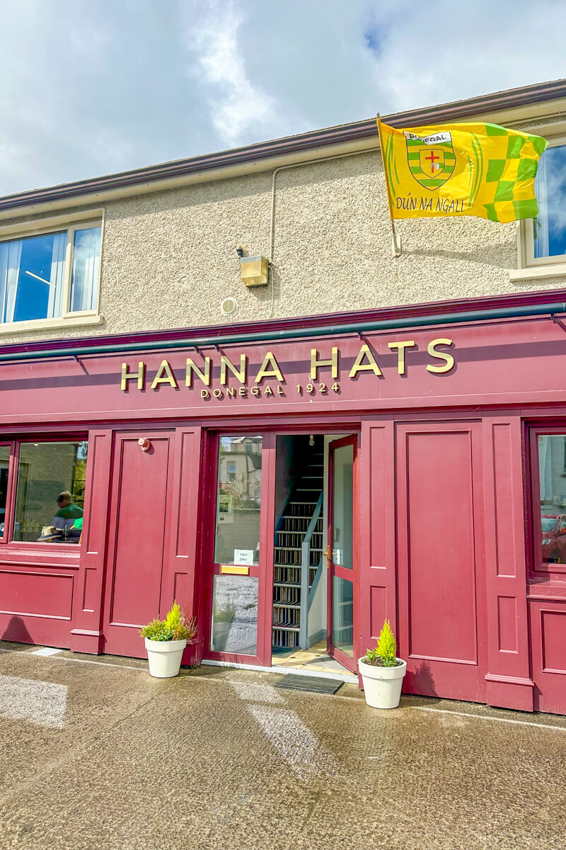 The red store front of Hanna Hats with the name in gold overhead. A yellow flag flies above.