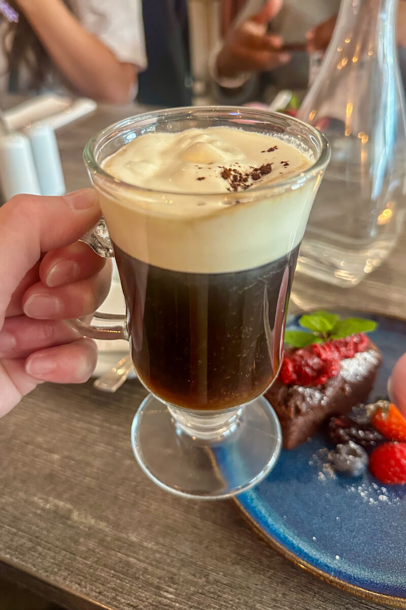 A hand holding up an Irish coffee in a clear glass