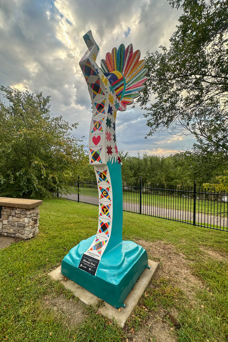 A small colorful copy of the Keeper of the Plains statue on some grass